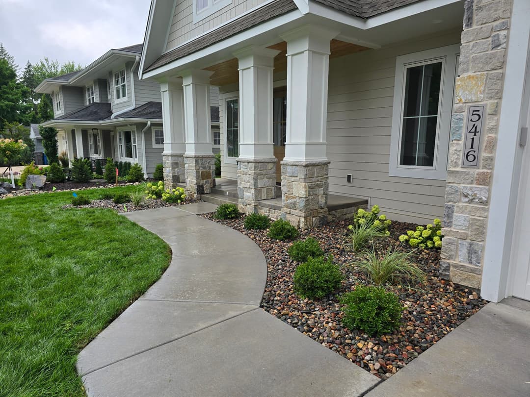 Modern suburban home entrance with landscaped path, greenery, and stone accents.