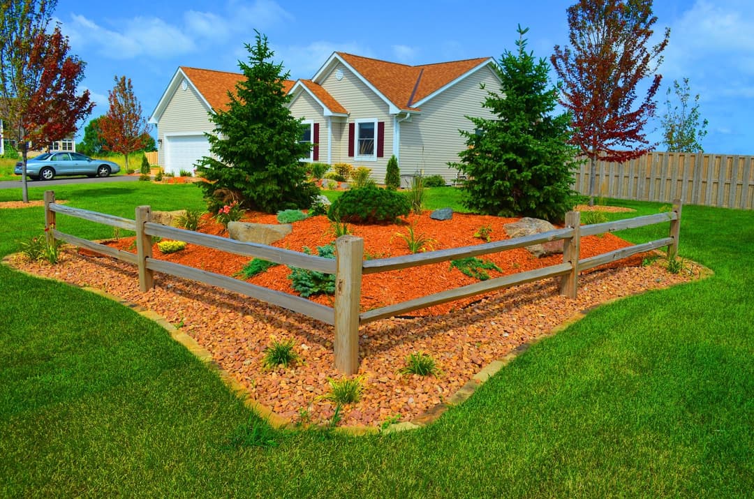 Colorful landscaped yard with red stone, green shrubs, and a charming home in the background.