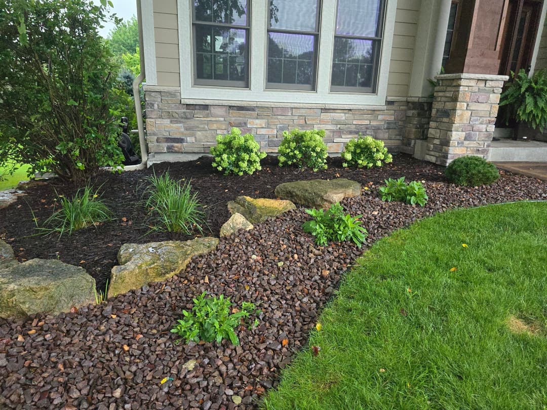 Attractive landscaping with stone borders, green plants, and mulch by a home entrance.