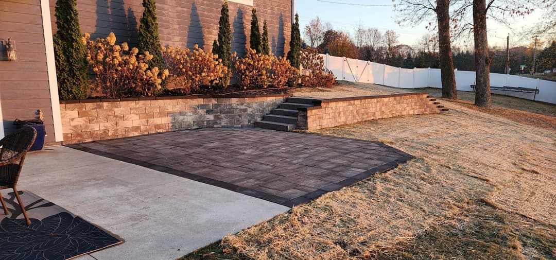 Paver patio with garden bed and steps leading to a landscaped yard at sunset.
