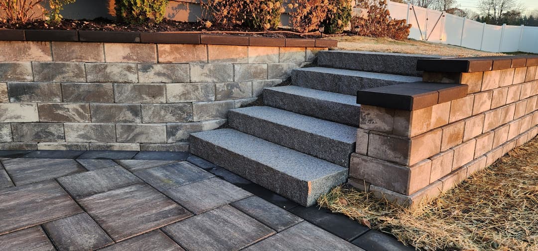 Granite steps leading up to a stone wall with landscaping in a residential area.