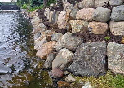 Natural stone wall along a lakeshore, with water, plants, and landscaping features visible.