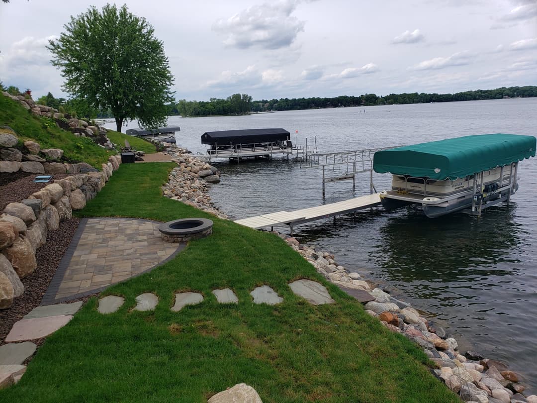 Lakeside view with docks, boats, stone path, and lush greenery under a cloudy sky.