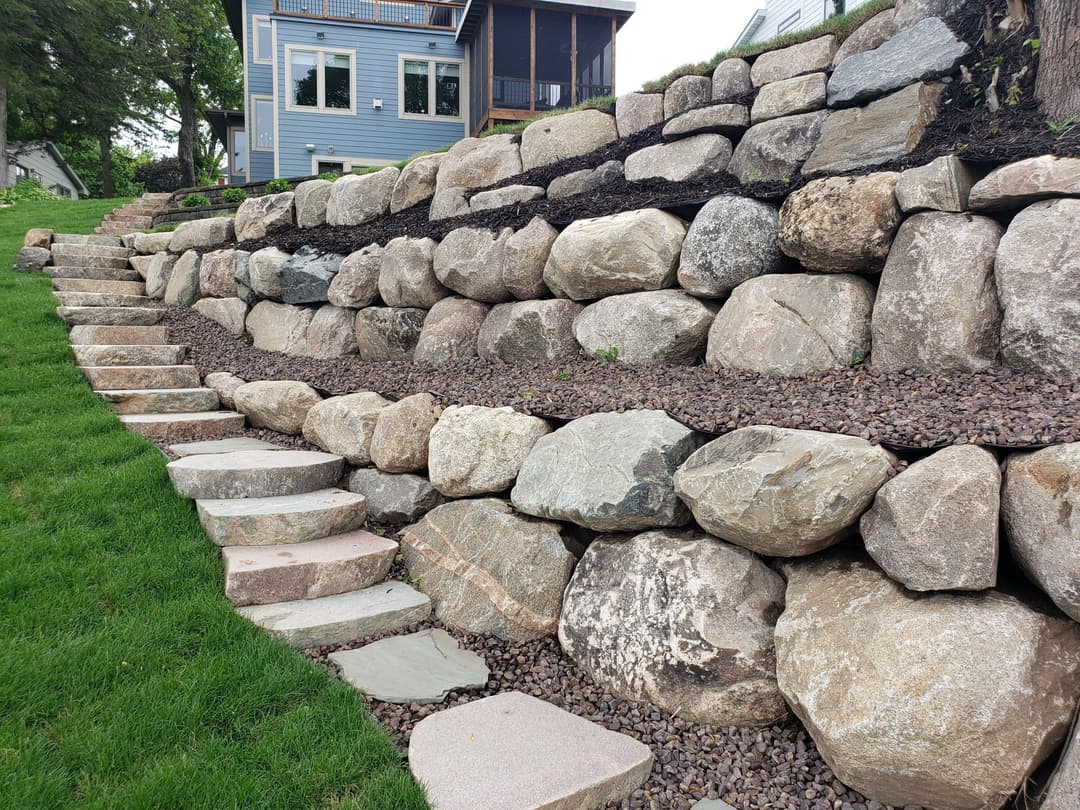 Landscape design featuring a stone retaining wall with steps and gravel in a backyard setting.