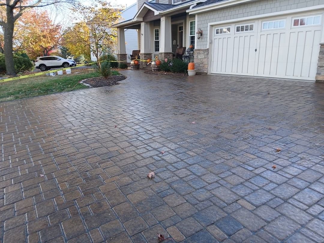 Patterned stone driveway with autumn decorations and a white car parked nearby.