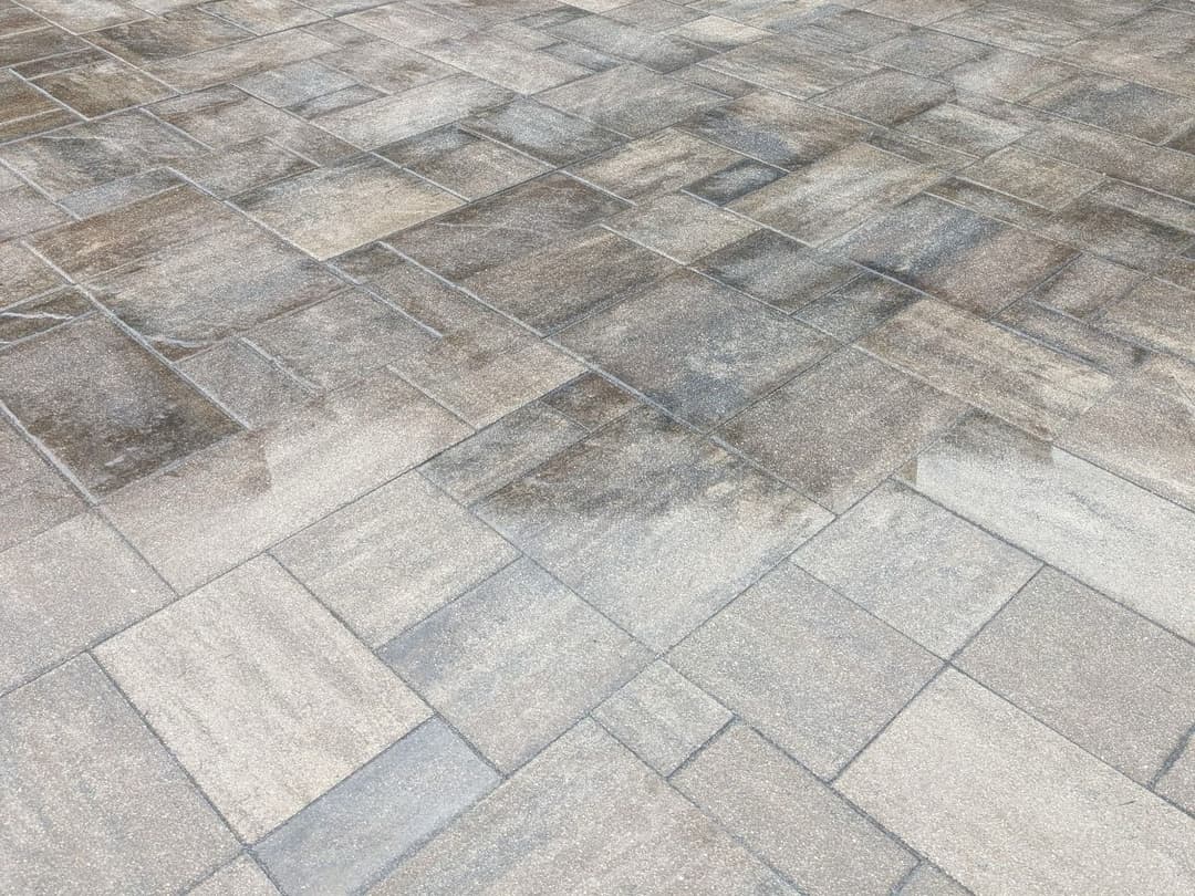 Textured stone patio surface with varied shades of gray and brown tiles in a geometric pattern.