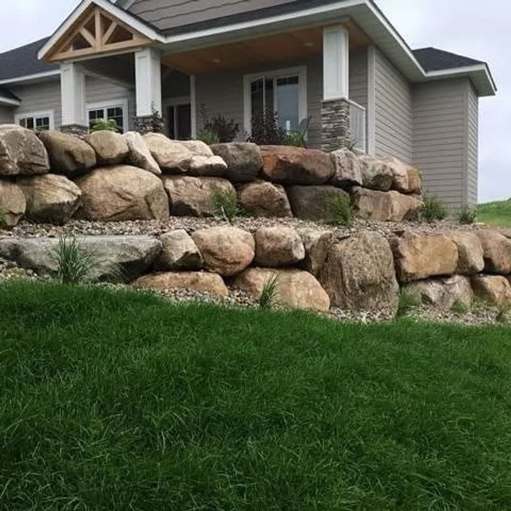 Residential home with stone landscaping and a manicured lawn, featuring a covered porch.