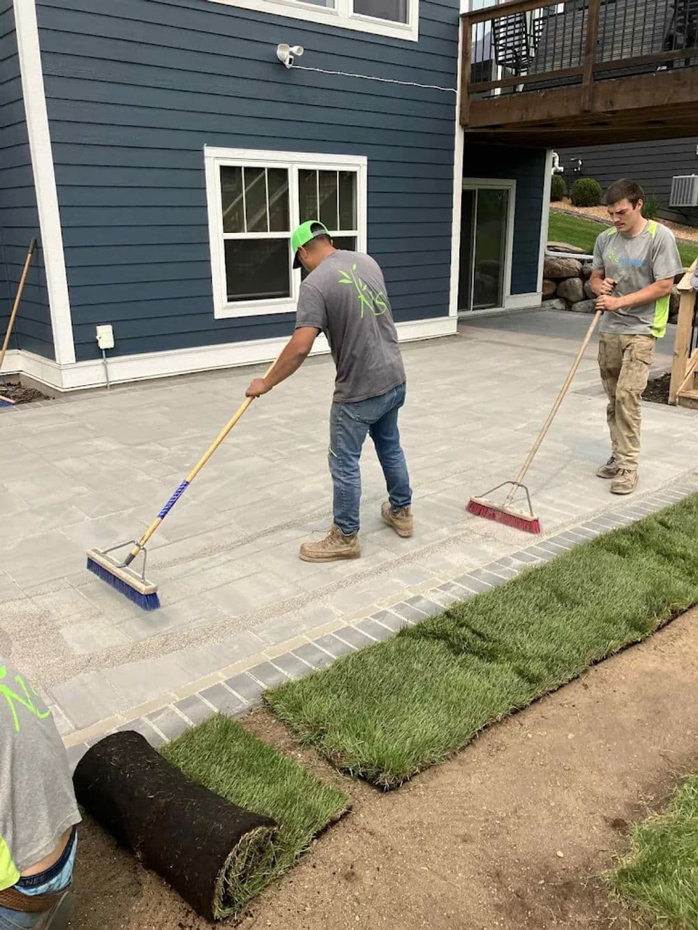 Workers laying pavers and installing sod in residential backyard landscape project.