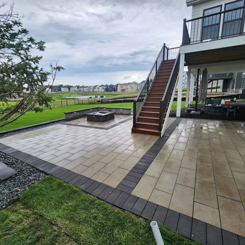 Modern outdoor patio featuring a fire pit, stairs, and green landscape under cloudy skies.