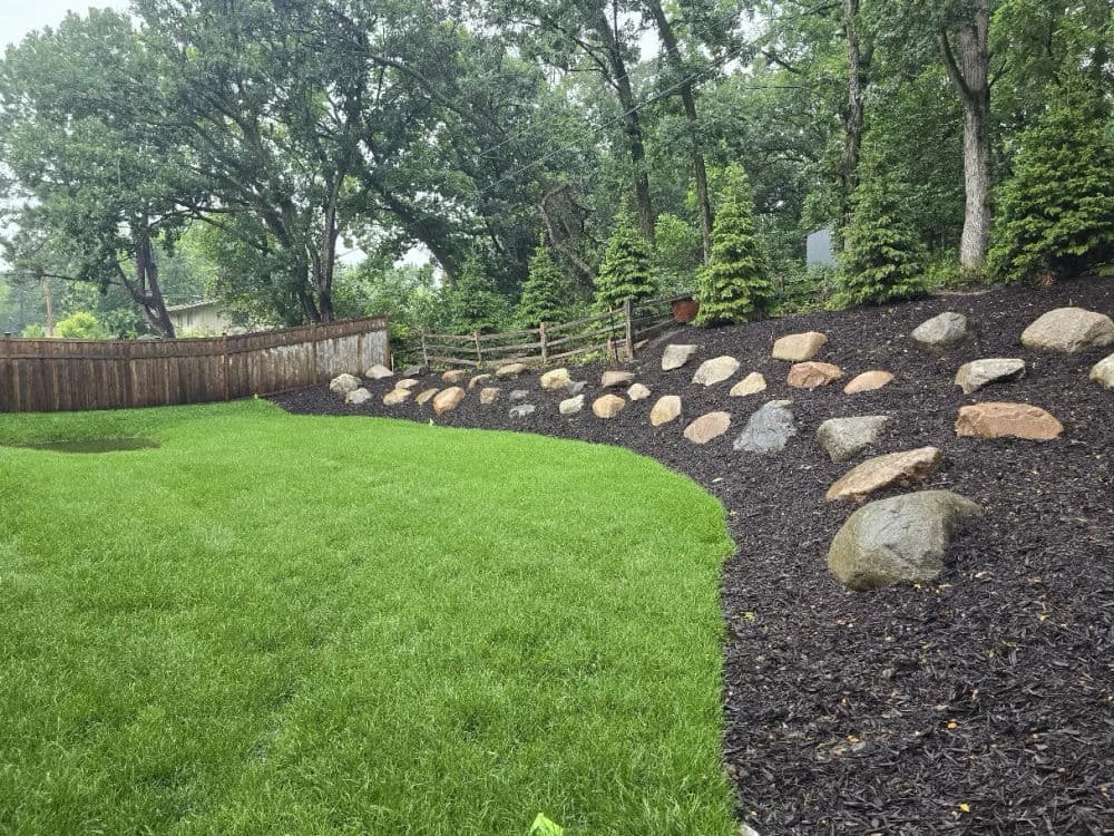 Lush green lawn with landscaped rocks and wooden fence in a serene backyard setting.