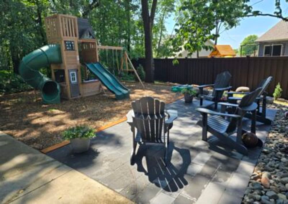 Backyard playground with slide and climbing structure, surrounded by outdoor seating area.