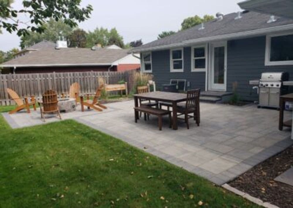 Backyard patio with seating area, grill, and outdoor dining table on stone pavers.