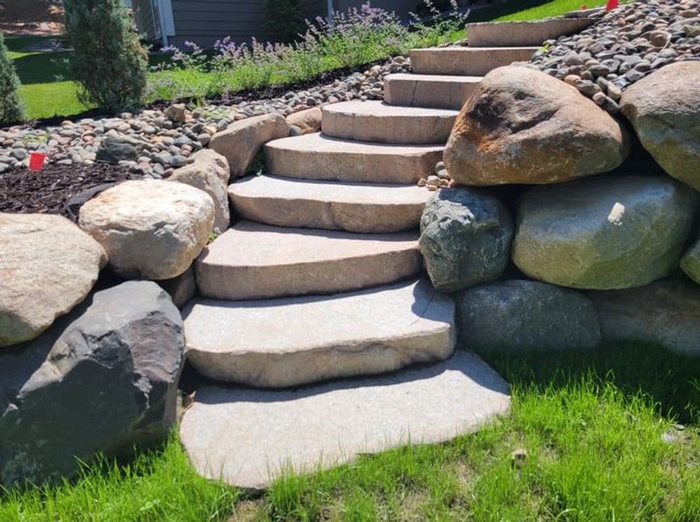 Stone staircase with large boulders and lush grass, enhancing garden landscape design.