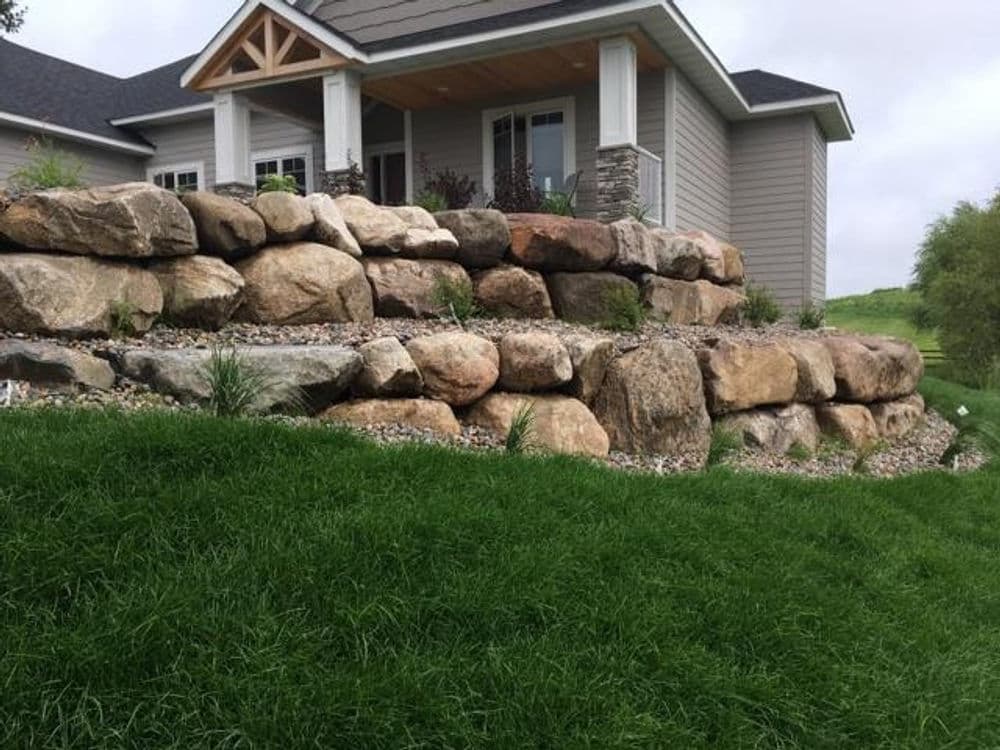 Stone retaining wall landscaping in front of a modern home with lush green grass.