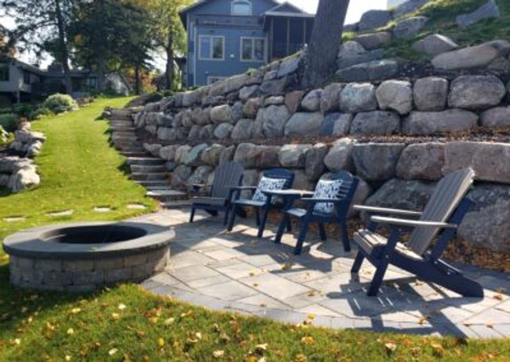 Cozy outdoor seating area with Adirondack chairs and a stone fire pit on a landscaped hill.