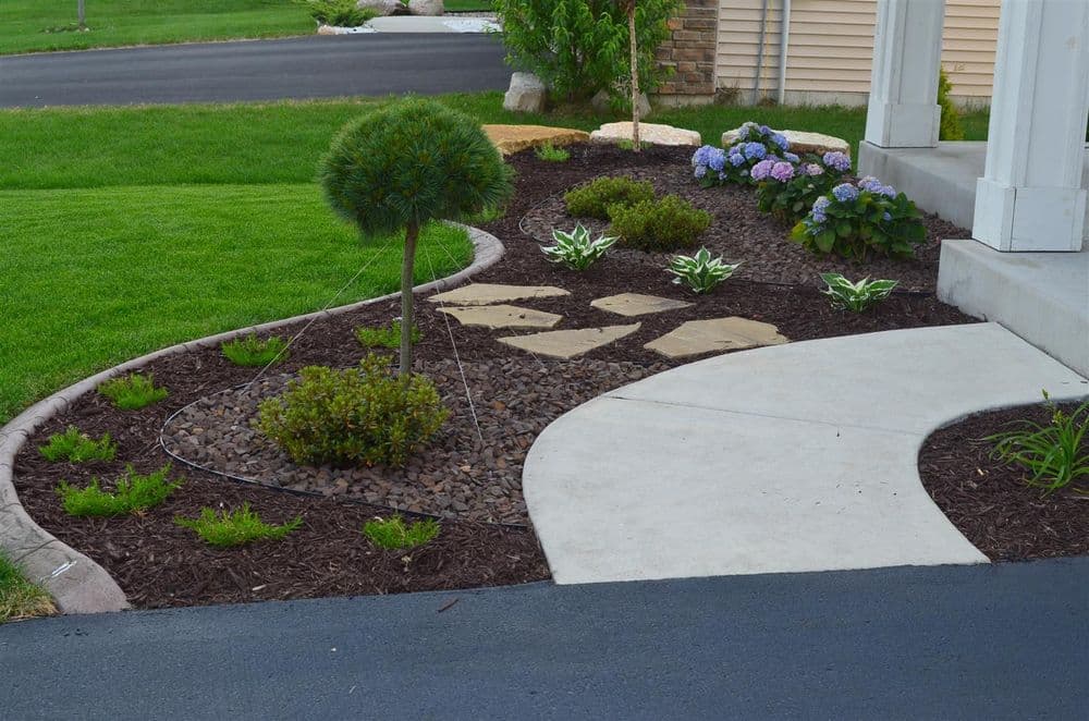 Lush garden landscape with stones, hydrangeas, and neatly trimmed bushes along a pathway.