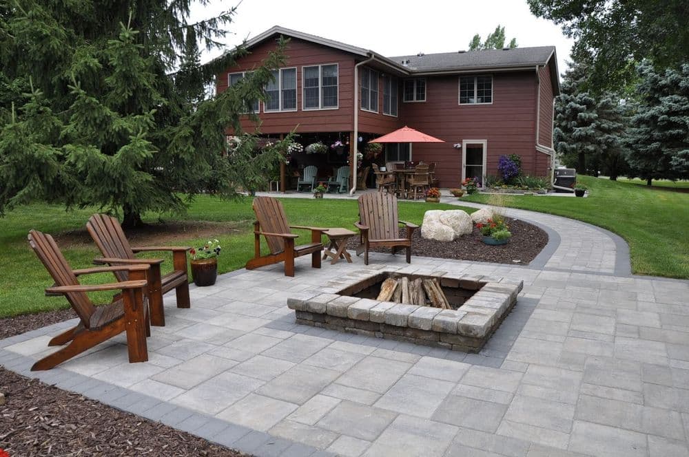 Cozy backyard patio with Adirondack chairs and a stone fire pit near a suburban home.