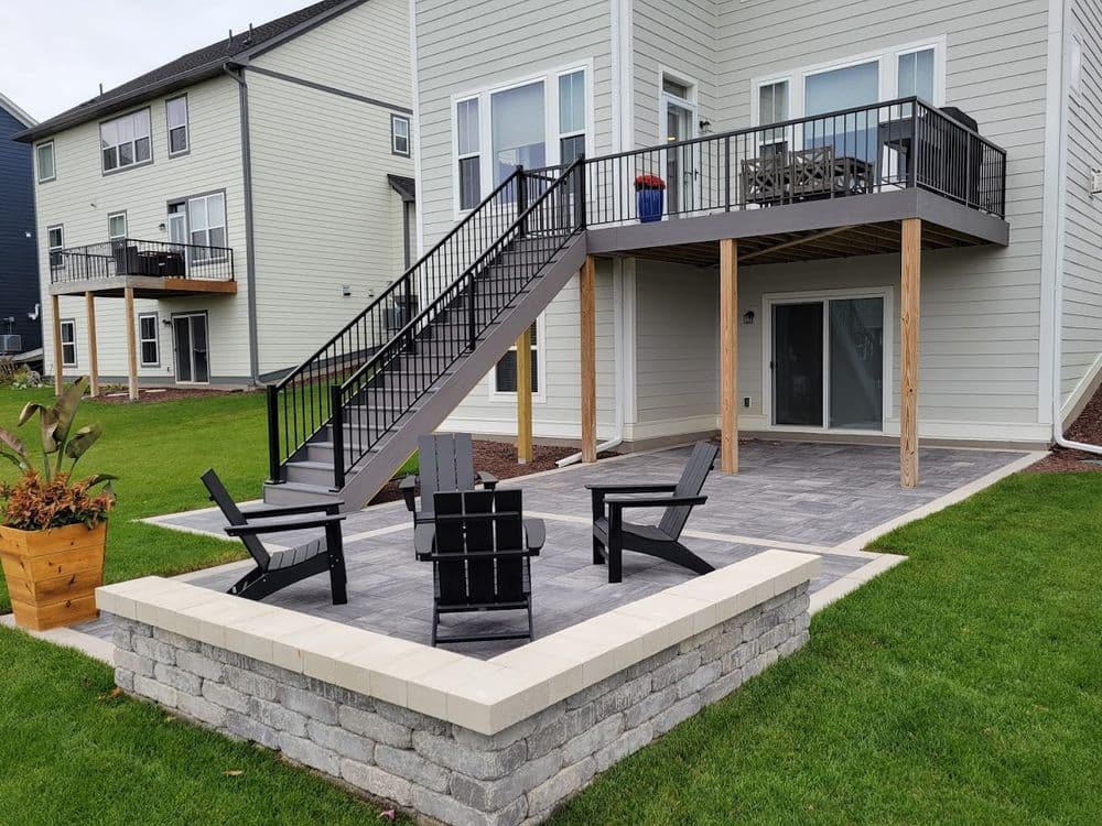 Modern backyard patio with seating area, stairs leading to upper deck, and landscaped lawn.