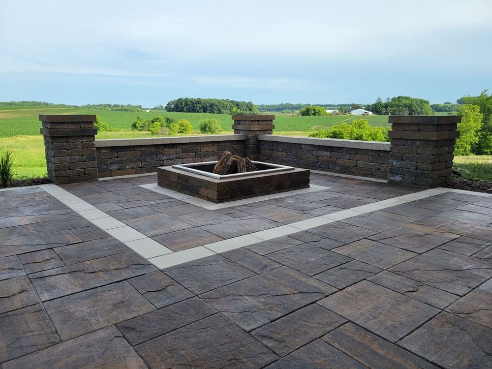 Stylish outdoor patio with a central fire pit and stone walls against a lush green landscape.
