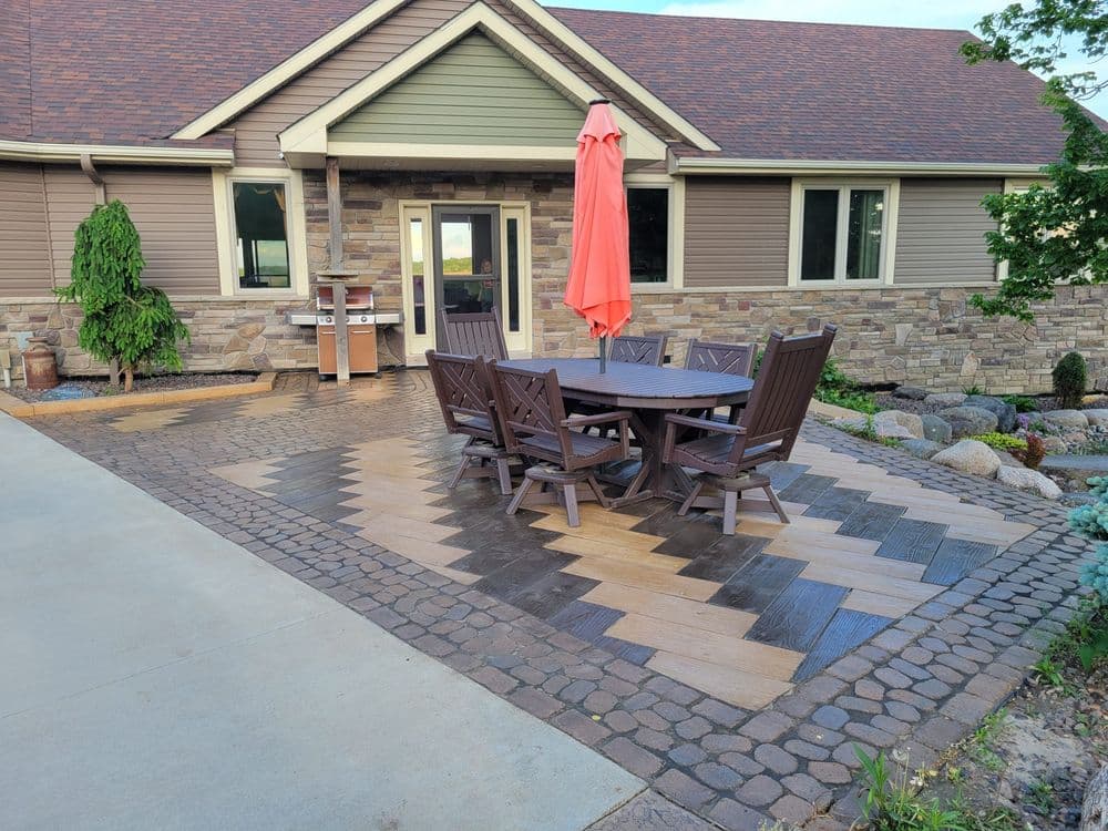 Outdoor patio with herringbone wood deck, stone walls, and a large umbrella over a dining table.