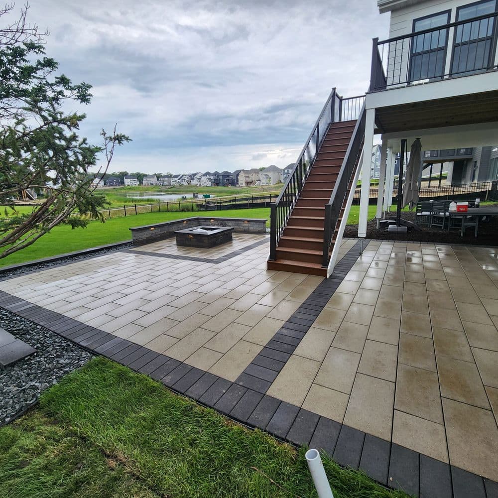 Patio with paver stone, fire pit, stairs, and grassy yard under a cloudy sky.