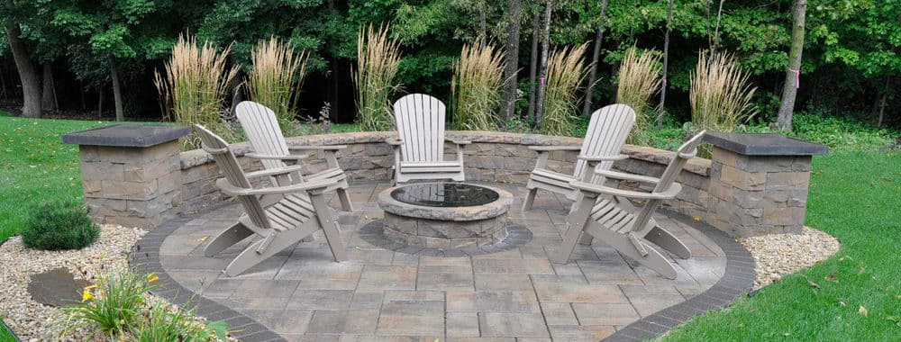 Outdoor seating area with four Adirondack chairs surrounding a fire pit amid lush greenery.