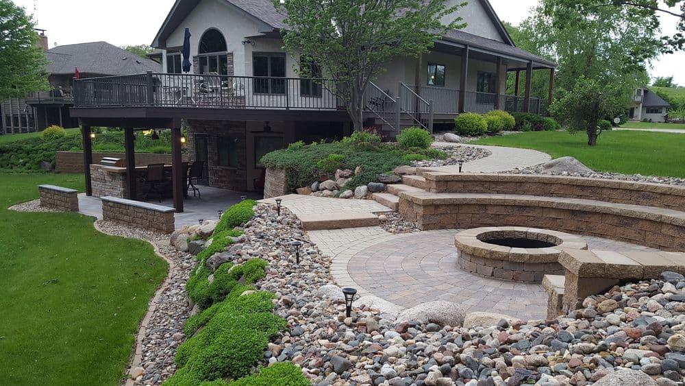 Beautiful landscaped backyard featuring a stone fire pit and winding brick pathways.
