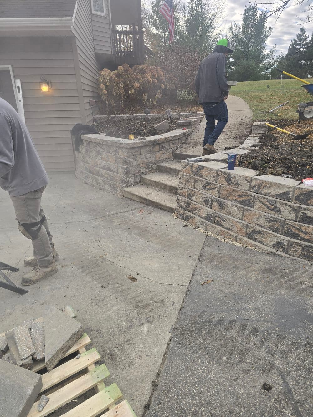 Stone stairs and patio construction with workers and tools in a residential yard.