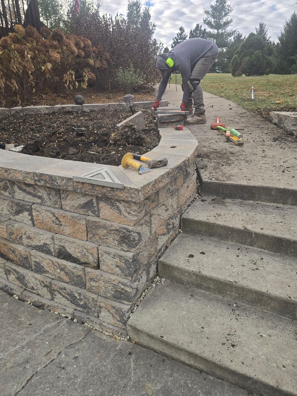 gardener working on stone garden bed with tools and plants in a landscaped area