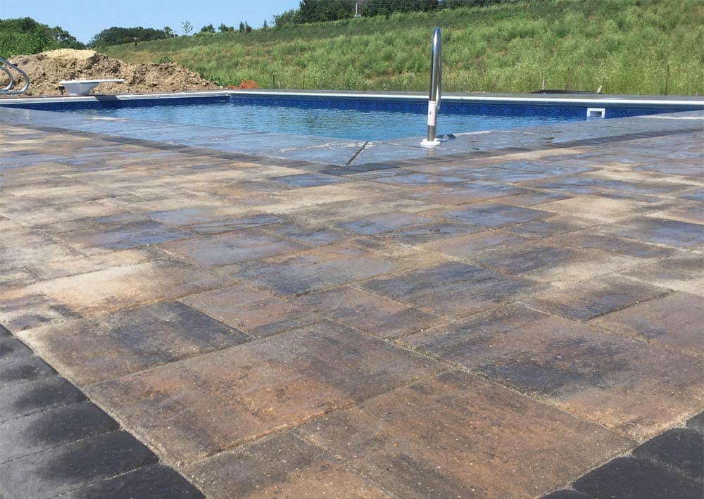 Newly constructed swimming pool with stone patio and green landscaping in the background.