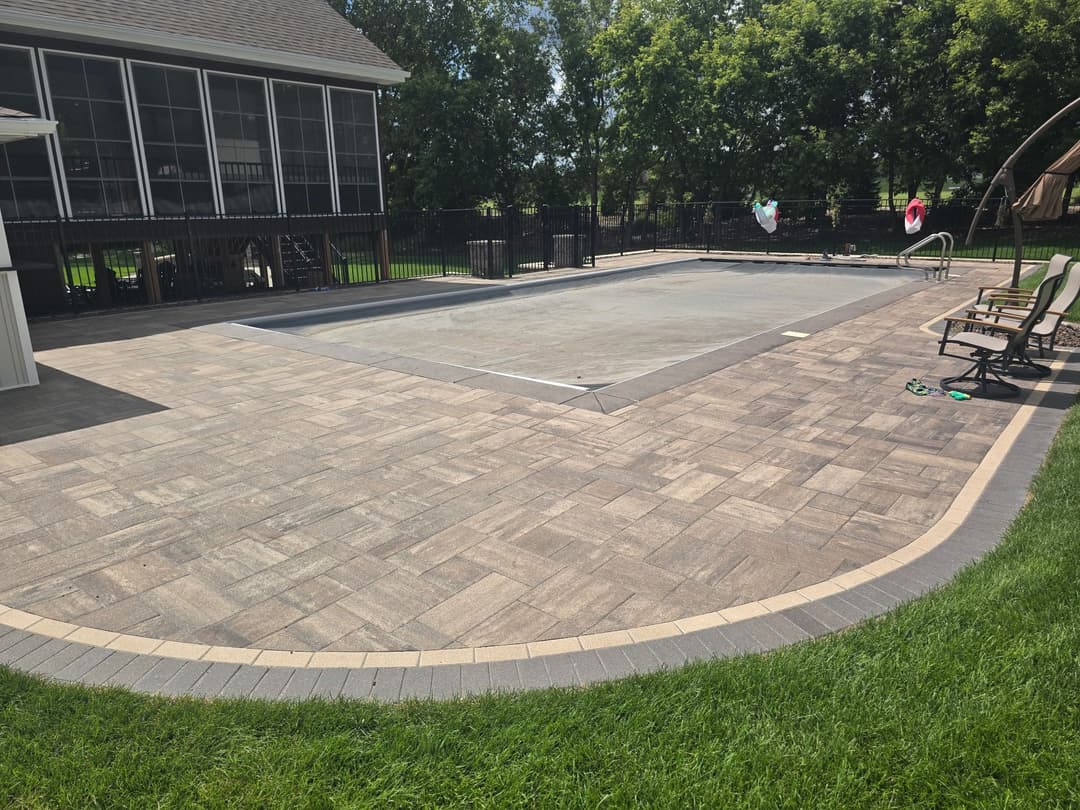 Inground pool surrounded by patio pavers, lush green lawn, and a screened porch in background.