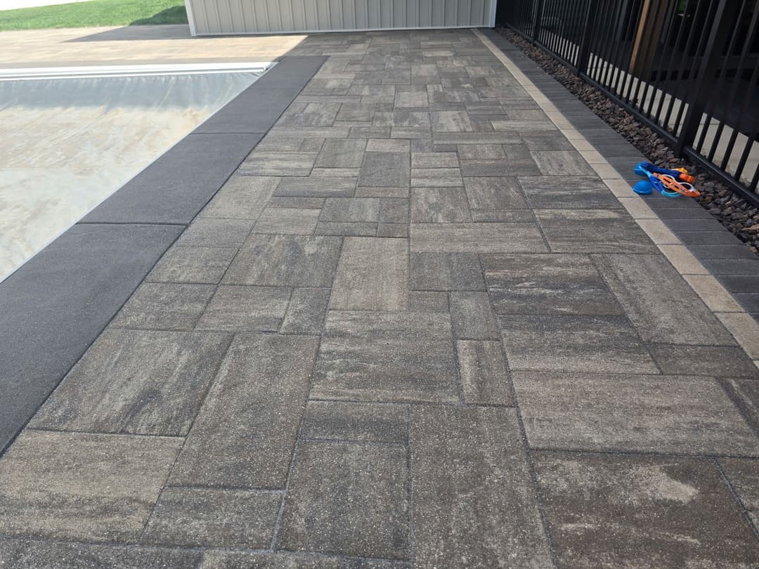 Paved poolside area with textured stones and a black fence, featuring pool construction tools.