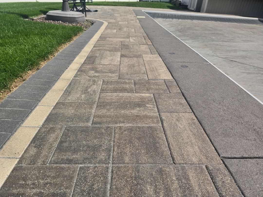 Paved walkway with modern stone design beside a lawn and pool area.