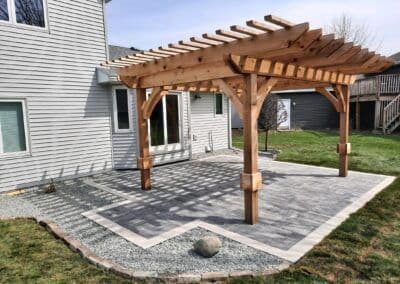 Wooden pergola with a stone patio in a backyard, enhancing outdoor living space.