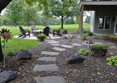 Stone path through a landscaped garden leading to a cozy seating area with Adirondack chairs.