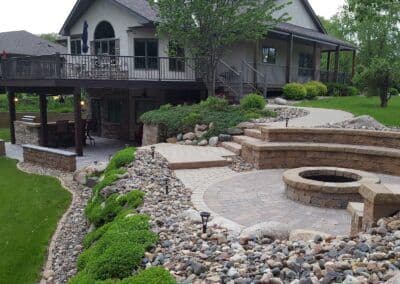 Elegant backyard with a stone patio, fire pit, and lush landscaping near a beautiful home.