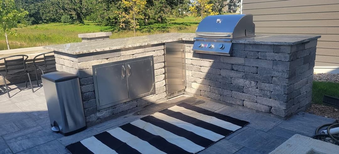 Outdoor kitchen with stone grill station, stainless steel appliances, and a stylish striped rug.